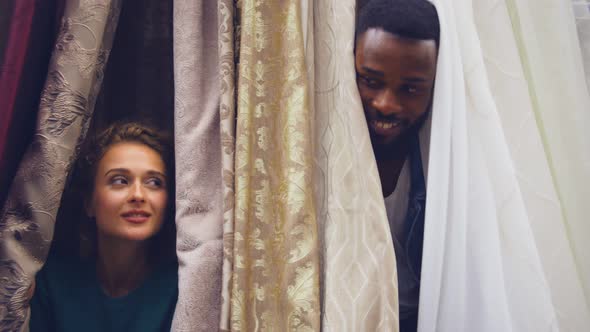 Happy Diverse Couple Shopping in Textile Store Having Fun and Hiding in Curtains
