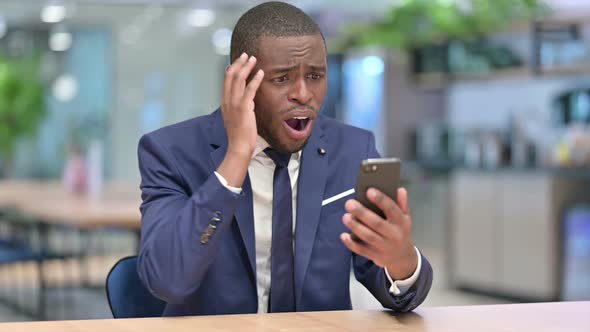 African Businessman Reacting to Failure on Smartphone in Office