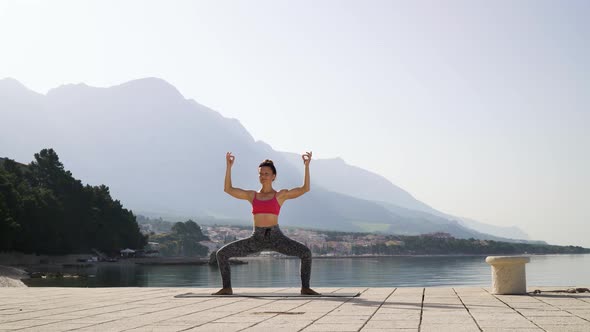 Adult Fit Woman Doing Yoga on Empty Sea Dock with Mountains on Background