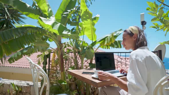 Side View Young Female Businesswoman Using Laptop Outdoors at Terrace with Palm Trees Remote Online