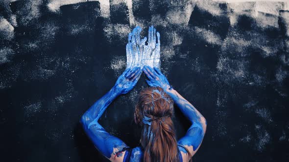 Attractive Hot Girl in a Blue Swimsuit Smeared with Blue Paint and Draws on the Wall