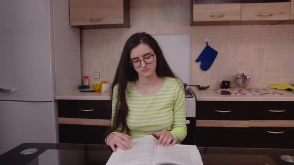 Pretty student preparing for an exam at home, sitting at a table with a textbook