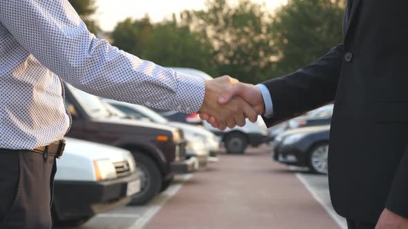 Two Businessmen Shaking Hands of Each Other with Cars in Parking at Background. Handshake Between