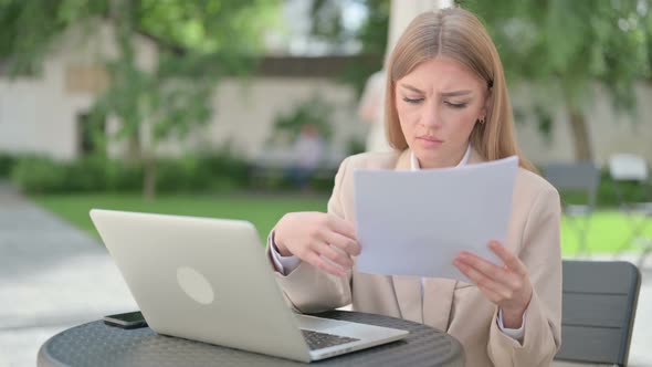 Young Businesswoman with Laptop Reading Documents in Outdoor Cafe