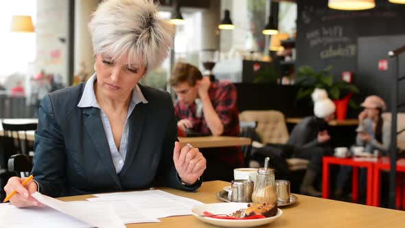 Middle Aged Woman Reads a Contract in Cafe, Coffee with Cake and Tablet