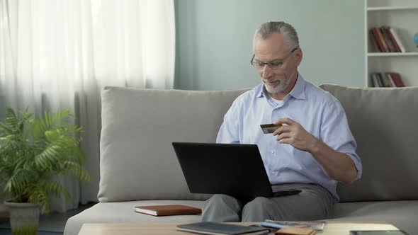 Pensioner Sitting on Sofa and Inserting Card Number on Laptop, Online Shopping