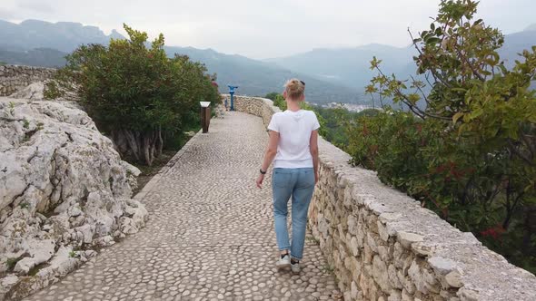 Blonde Girl Walks on Defensive Walls of Medieval Castle in Europe Mountains