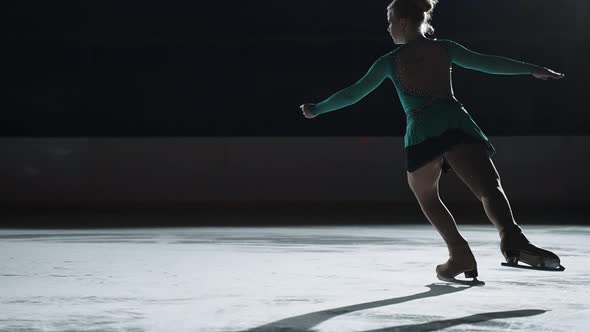 The Girl Skater Performs a Jump with the Rotation of a Triple Toe Loop in a Counter Light on an Ice