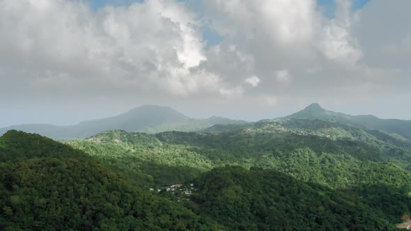 Drone camera shoots wooded mountains with settlement on top and foggy clouds (Saint Lucia)