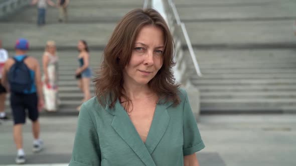 Portrait of a Middle-aged Woman in a Dress Walking Down the Street on the Background of Stairs with