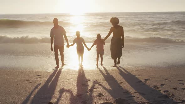 Smiling african american family walking and holding hands on sunny beach