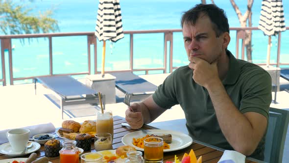 Sad Thoughtful Man Touches Face Touch Chin By Hand Have Breakfast at Restaurant in Hotel Turquoise