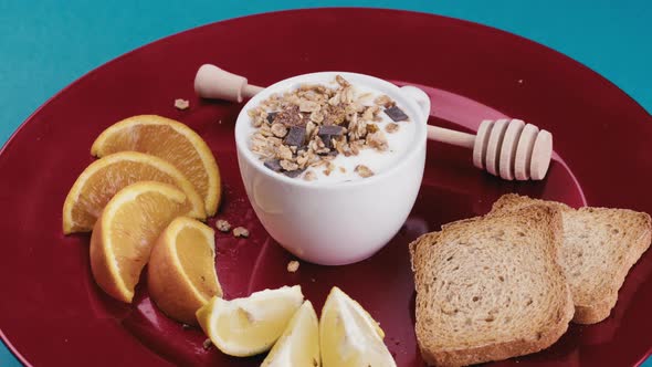 Cup of Fresh White Yogurt with Crunchy Granola Inside Rotates in a Red Plate