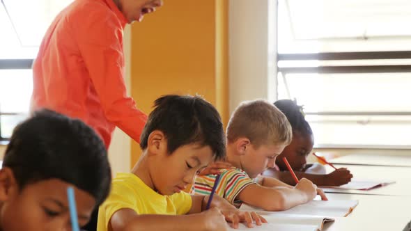 Teacher assisting school kids with their classwork in classroom