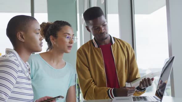 Diverse male and female creative colleagues in discussion standing together at laptop