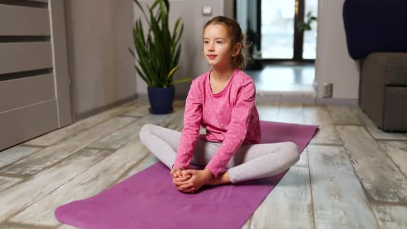 Little girl doing stretching exercises, practicing yoga on fitness mat at home