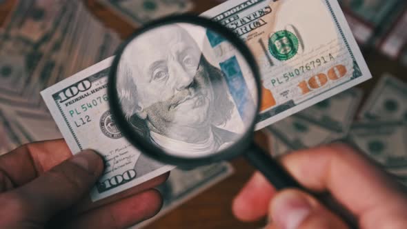 One Hundred Dollars Inspecting Under Magnifying Glass on Money Background