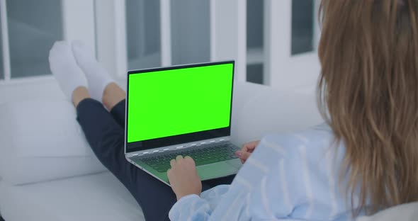 A Young Woman Sits with a Laptop on Her Lap with a Green Screen During Quarantine. Chromakey on the
