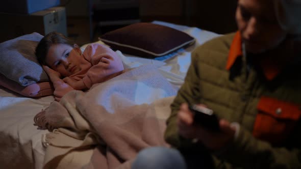 Portrait of Depressed Child Lying in Silence on Mattress in Bomb Shelter Watching Woman Walking Away