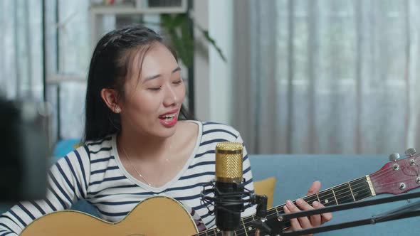 Close Up Of Asian Woman Singing And Playing A Guitar While Live Stream At Home