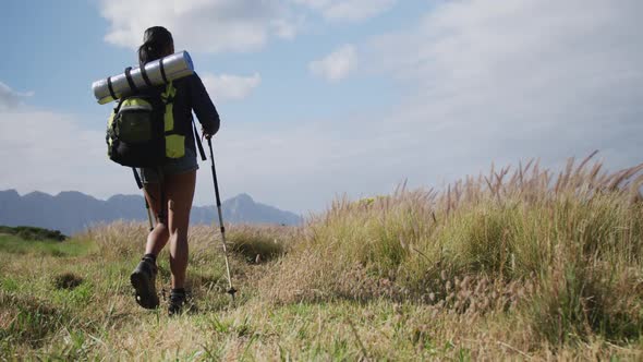 Mixed race woman wearing backpack using nordic walking poles hiking in countryside