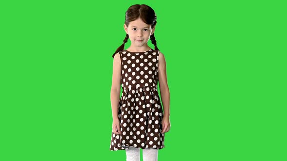 Little Girl in Polka Dot Dress with Pig Tails Walking and Smiling Shyly To the Camera on a Green