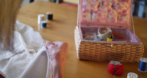 An old woman sewing a new button onto a white shirt by hand to repair it with her needle and thread.