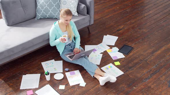 Young woman works with documents using a laptop at home.