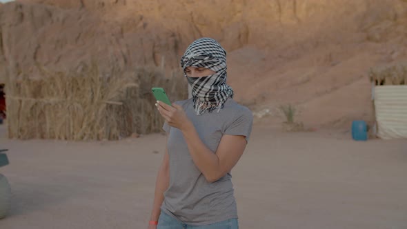 Female Tourist in Checkered Keffiyeh Standing in the Desert Using Mobile Phone