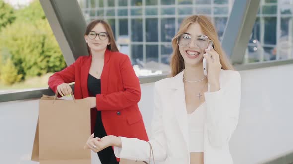 Happy girl in a suit in sunglasses with shopping bags on a city street. Young lady standing on stree