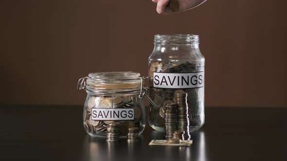 Hand of Man Putting Money Into Glass with Savings