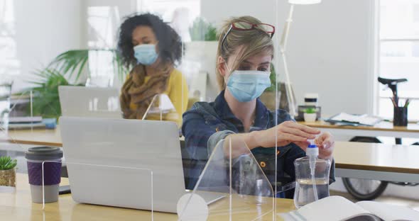 Woman wearing face mask sanitizing her hands at office