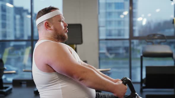 Fat Burning Overweight Man Lifting Blocks on Rowing Machine Training on Block Device and Gym