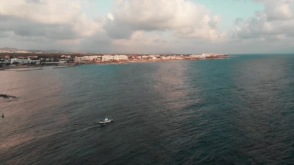 Drone view of white fishing boat sails out of city marina into mediterranean wavy sea at sunset 