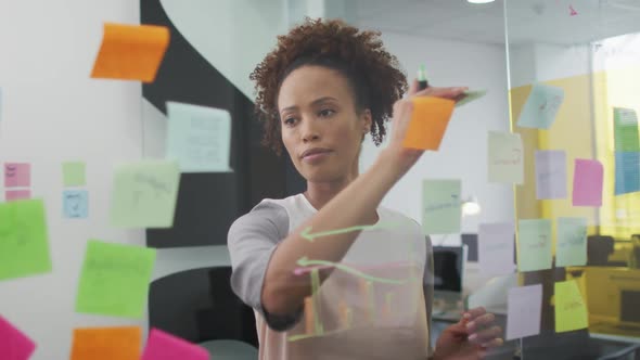 Mixed race businesswoman brainstorming, drawing with green marker on transparent board