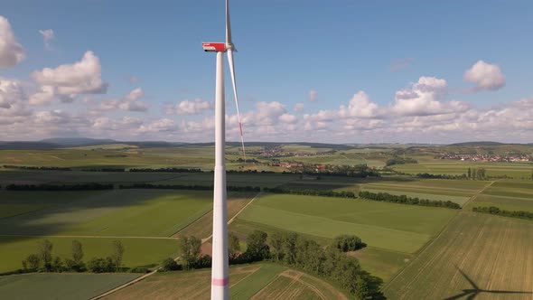Tall, white and red wind turbine spinning in front of German countryside and a vibrant sky with few