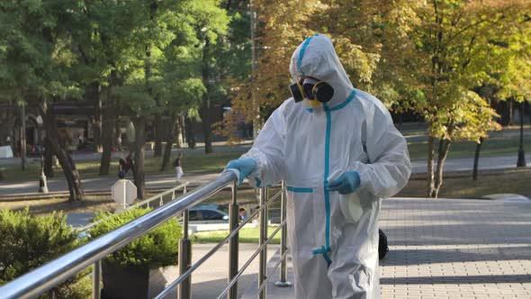 A Virologist in Protective Clothing Disinfects the Railing with an Antiseptic Spray and a Tissue