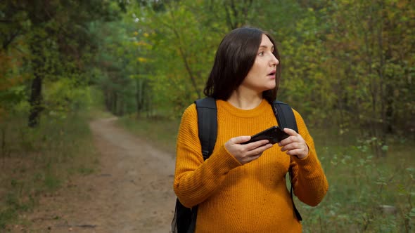 Tired Woman Tourist Reads Map on Phone Walking Along Forest