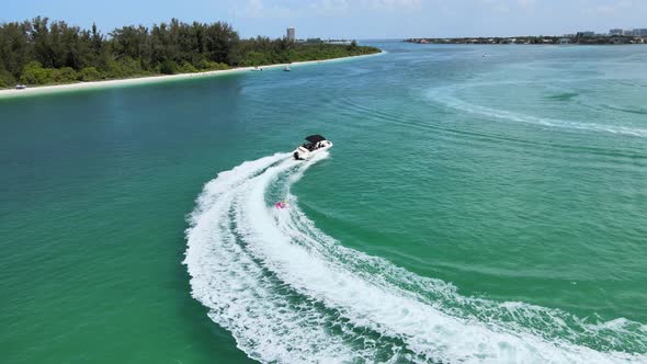 Camera moves in a circle around a speed boat pulling a towable in an ocean near a beach.