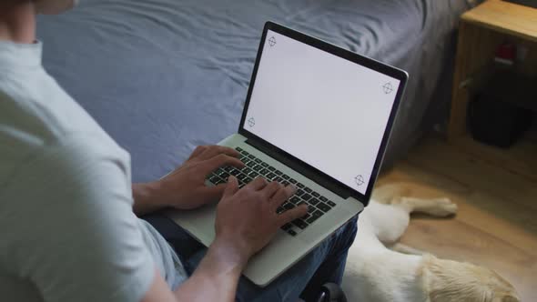Caucasian man using laptop in bedroom with pet dog