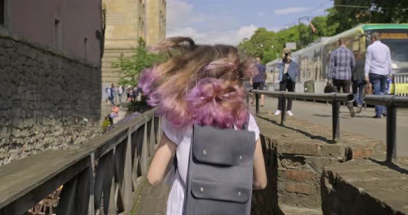 Young Woman with Backpack and Purple Hair Running in Old City, Back View