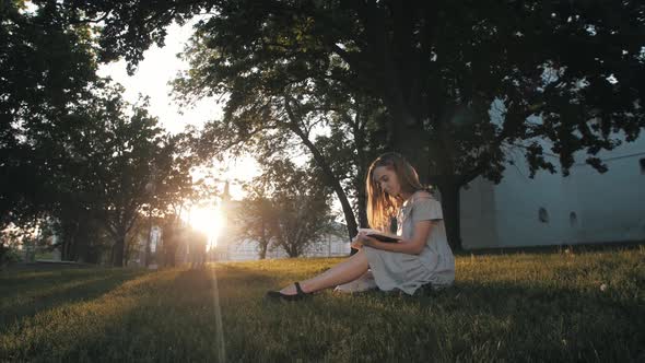 Woman in Dress Reads the Book in Sun Lights at Sunset