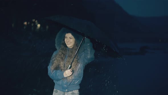 Happy Girl Jumps Holding Umbrella Under Spring Rain at Night