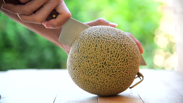 The man use knife split the green melon on wood plate