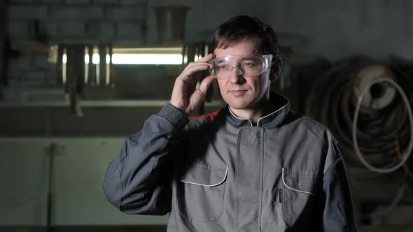 Portrait worker in safety glasses. man stands at factory and looks at camera.