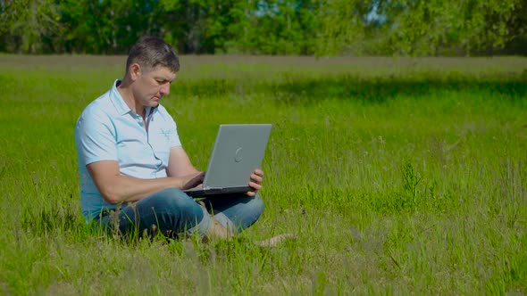 Businessman Works Behind a Laptop Sitting on the Grass