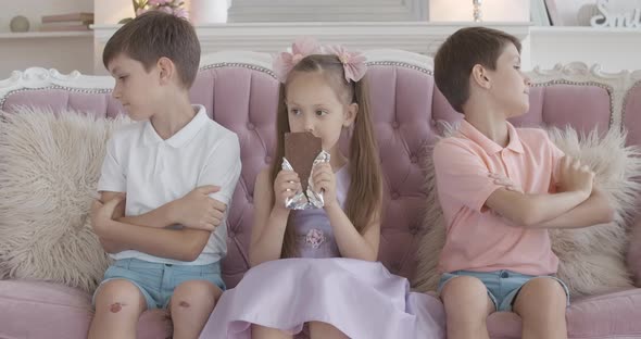 Portrait of Greedy Little Girl Chewing Chocolate Bar As Brothers Sitting on Both Sides with Hands