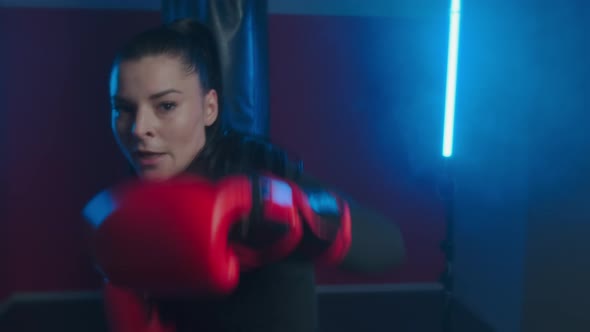 Beautiful woman kickboxer beats with fists in boxing gloves towards the camera, dodging punches