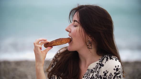 Smiling Brunette Woman Posing with a Bagel on the Beach