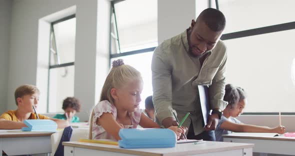 Video of happy african american male teacher helping in exercise to caucasian girl